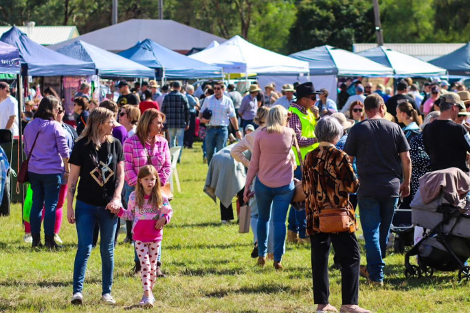 A crowd of people walking through a market with stall tents in the background